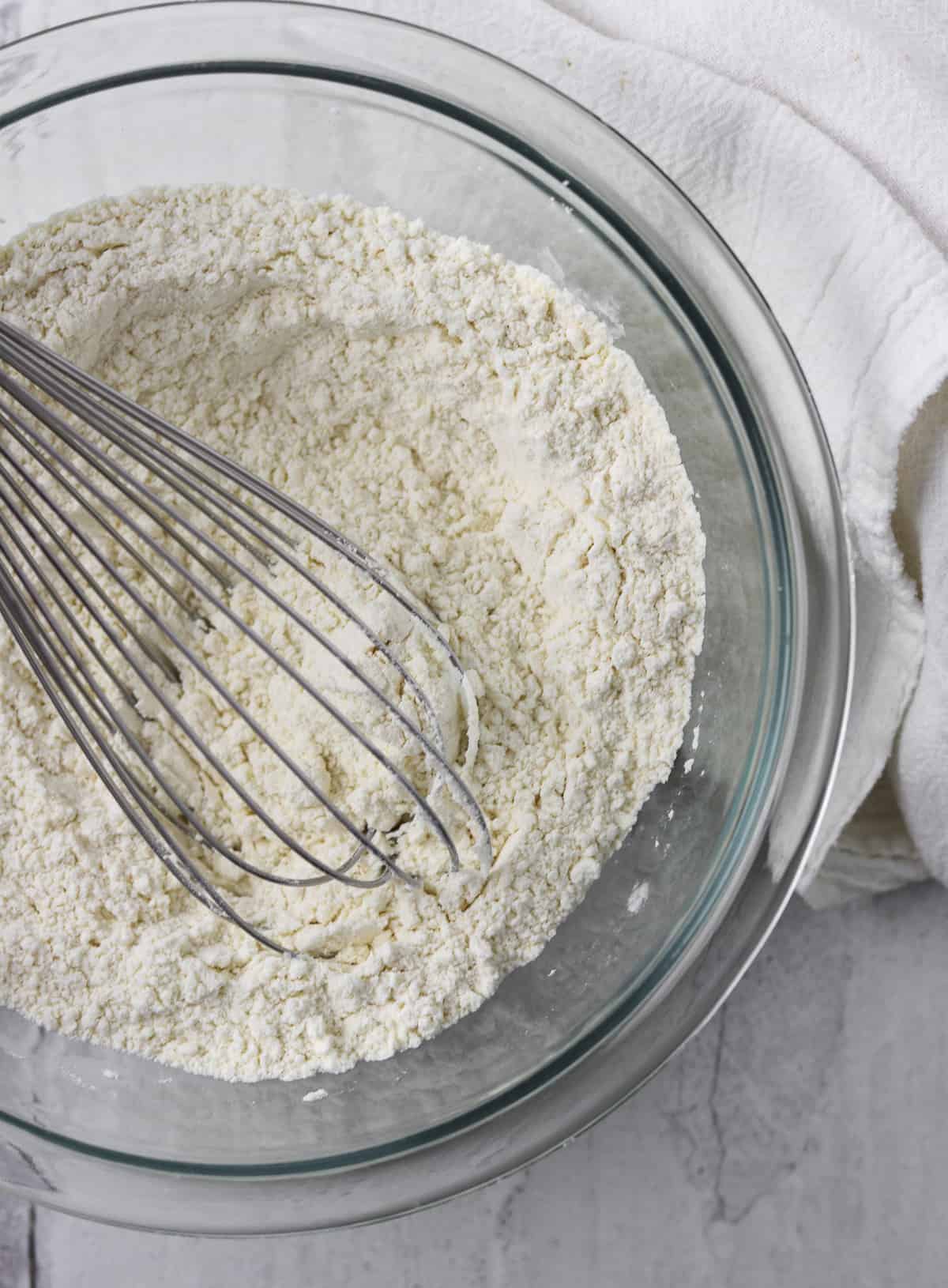 flour in a bowl with a whisk next to a towel.
