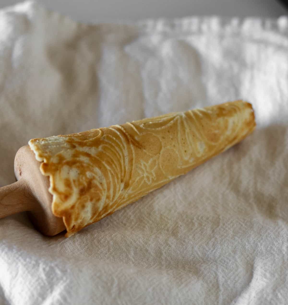 Krumkake cookie wrapped around a wooden cone form on a towel.