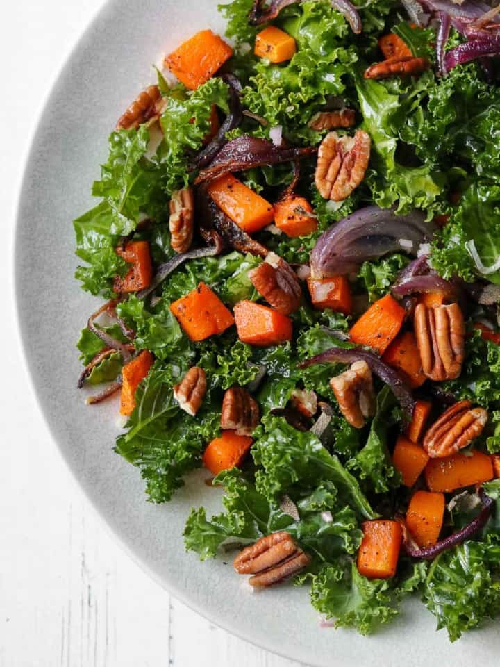 Kale salad with roasted butternut squash and pecans on a plate.