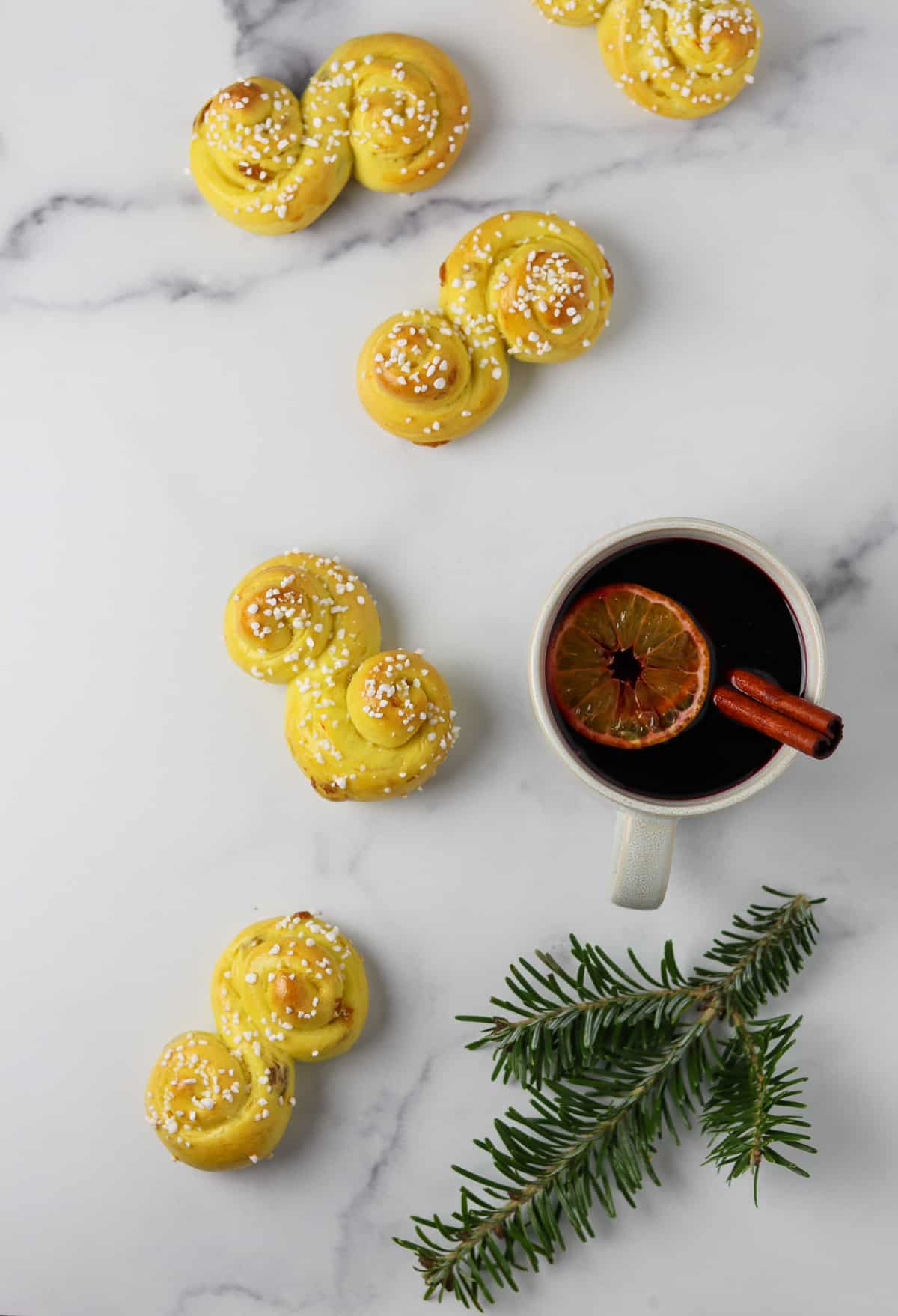 St. Lucia Buns on a marble surface next to a mug of mulled wine and a pine branch.