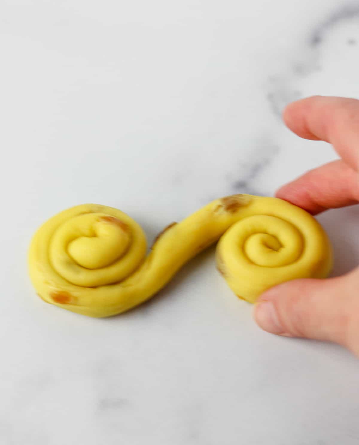 Saffron bun dough coiled up on a marble surface.