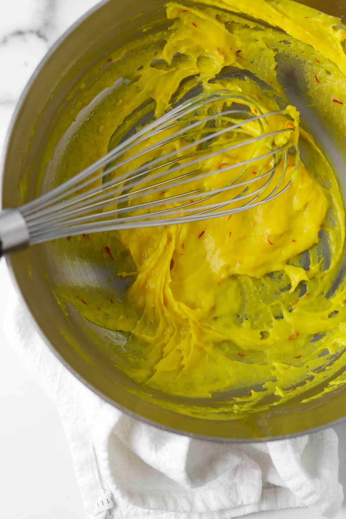Yellow saffron dough in a pan with a whisk.