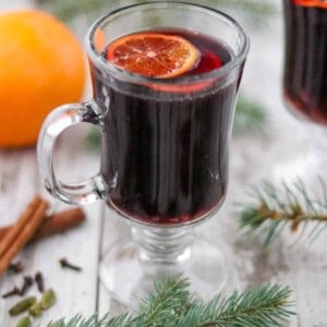 A cup of mulled wine next to evergreen branches, spices and an orange.
