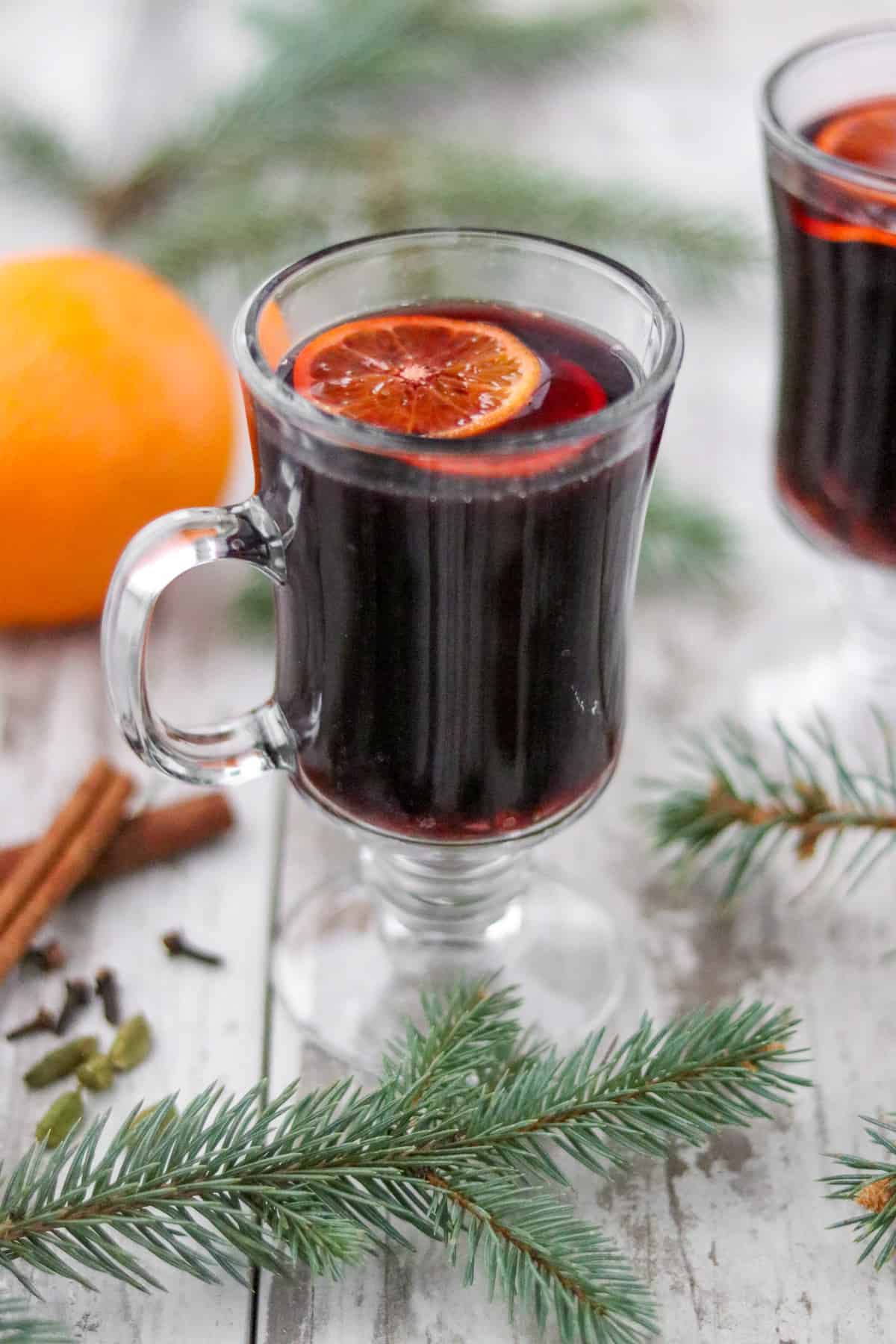 A cup of mulled wine next to evergreen branches, spices and an orange.