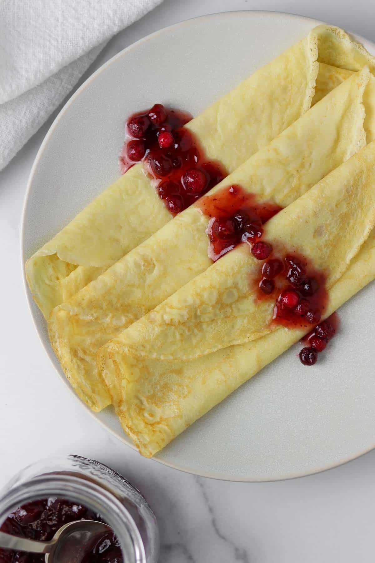 Swedish pancakes on a plate drizzled with lingonberries.