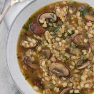 Close up of a bowl of mushroom and barley soup next to a spoon.