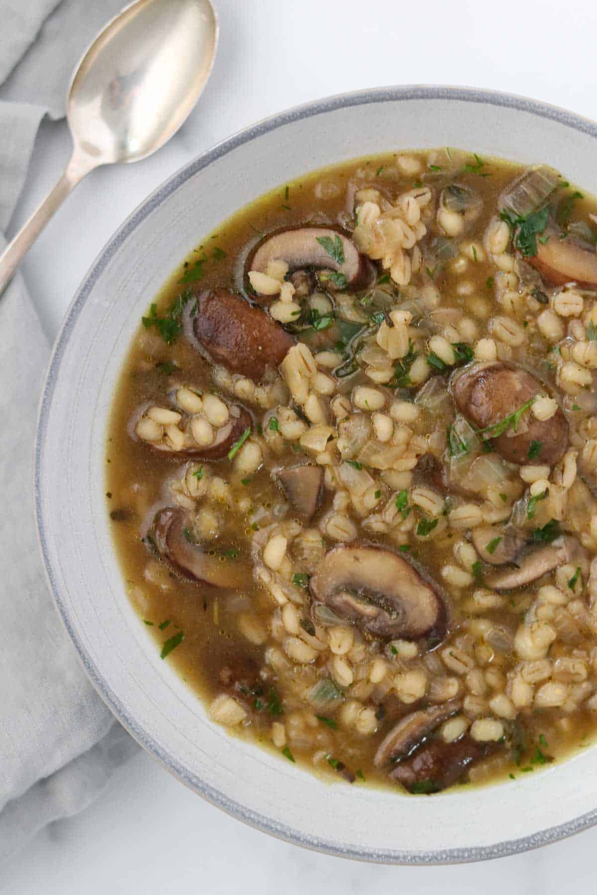 Close up of a bowl of mushroom and barley soup next to a spoon.