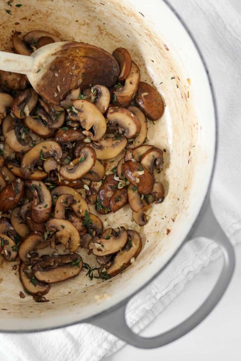 Cooked mushrooms in a pot with a wooden spoon.