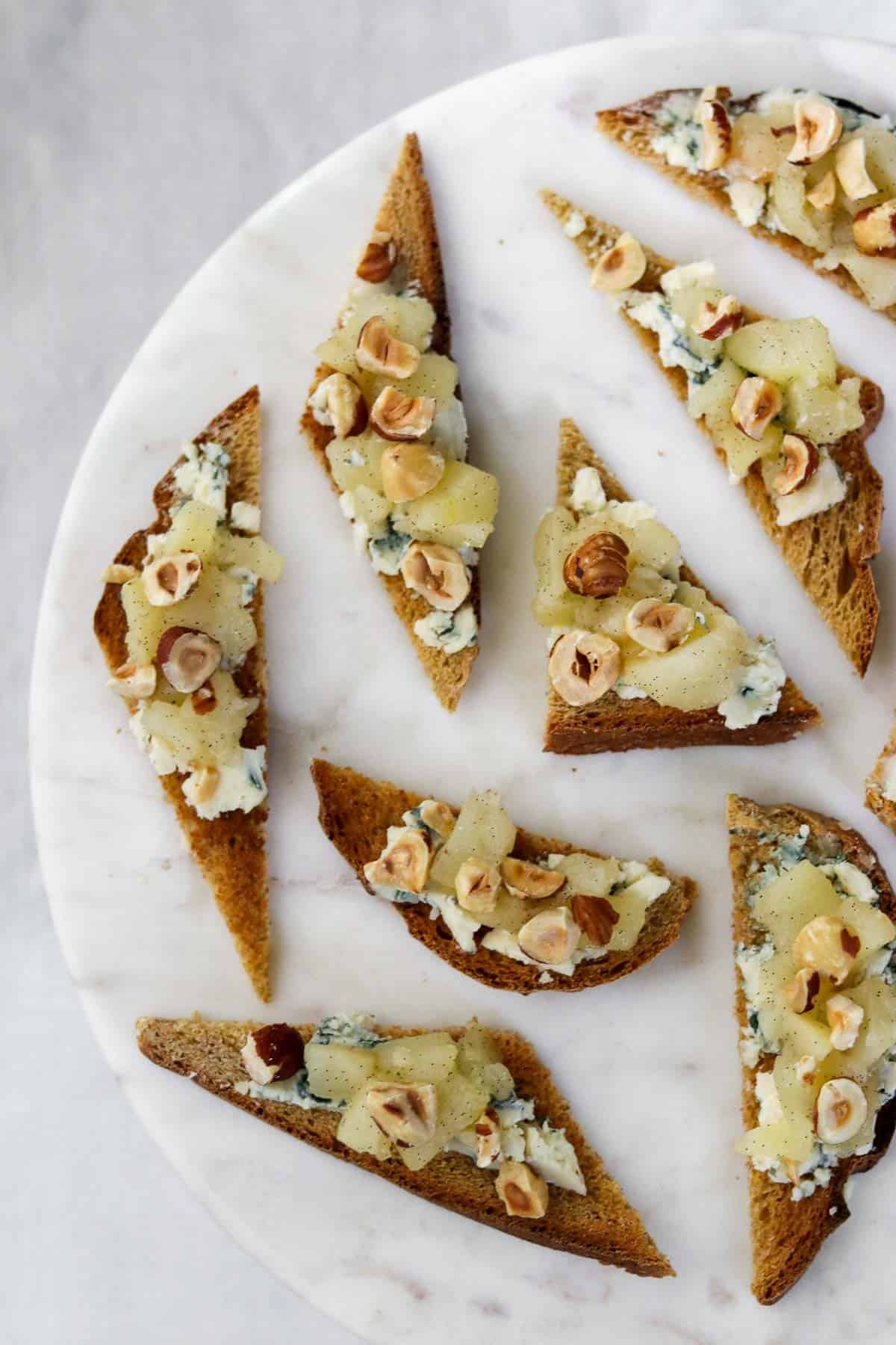 Toasts with blue cheese, pears and hazelnuts on a marble plate.