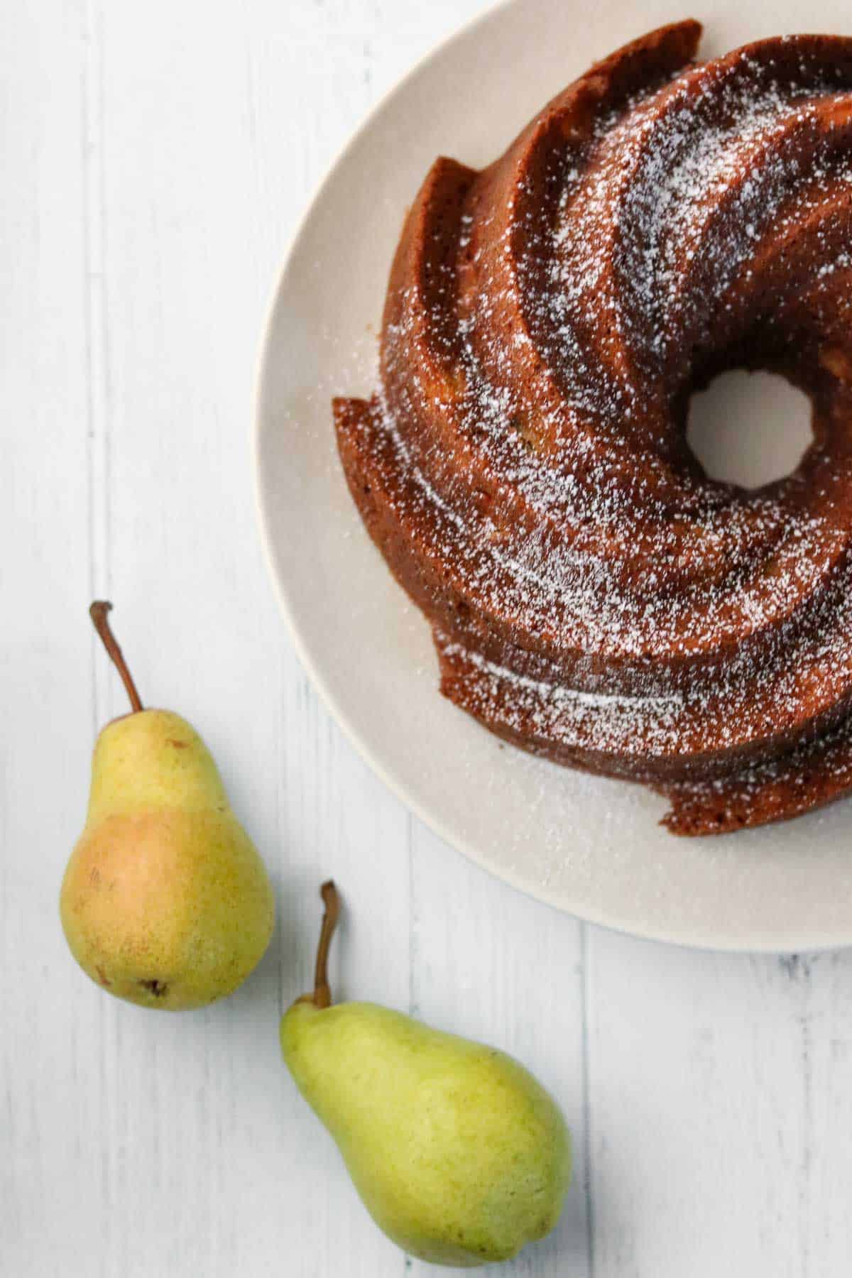 Bundt cake on a plate next to two pears.