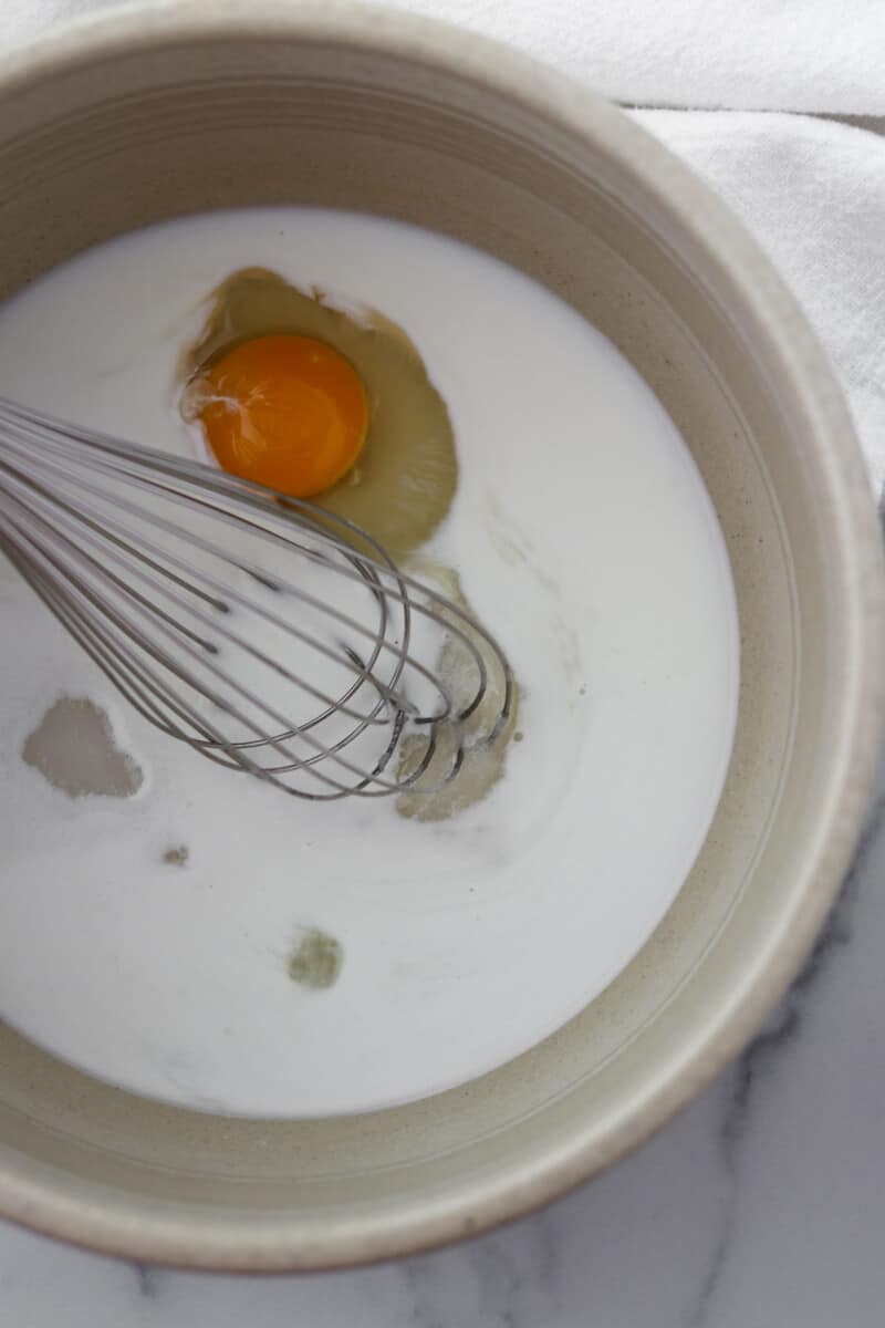 Milk and egg in a bowl with a whisk.