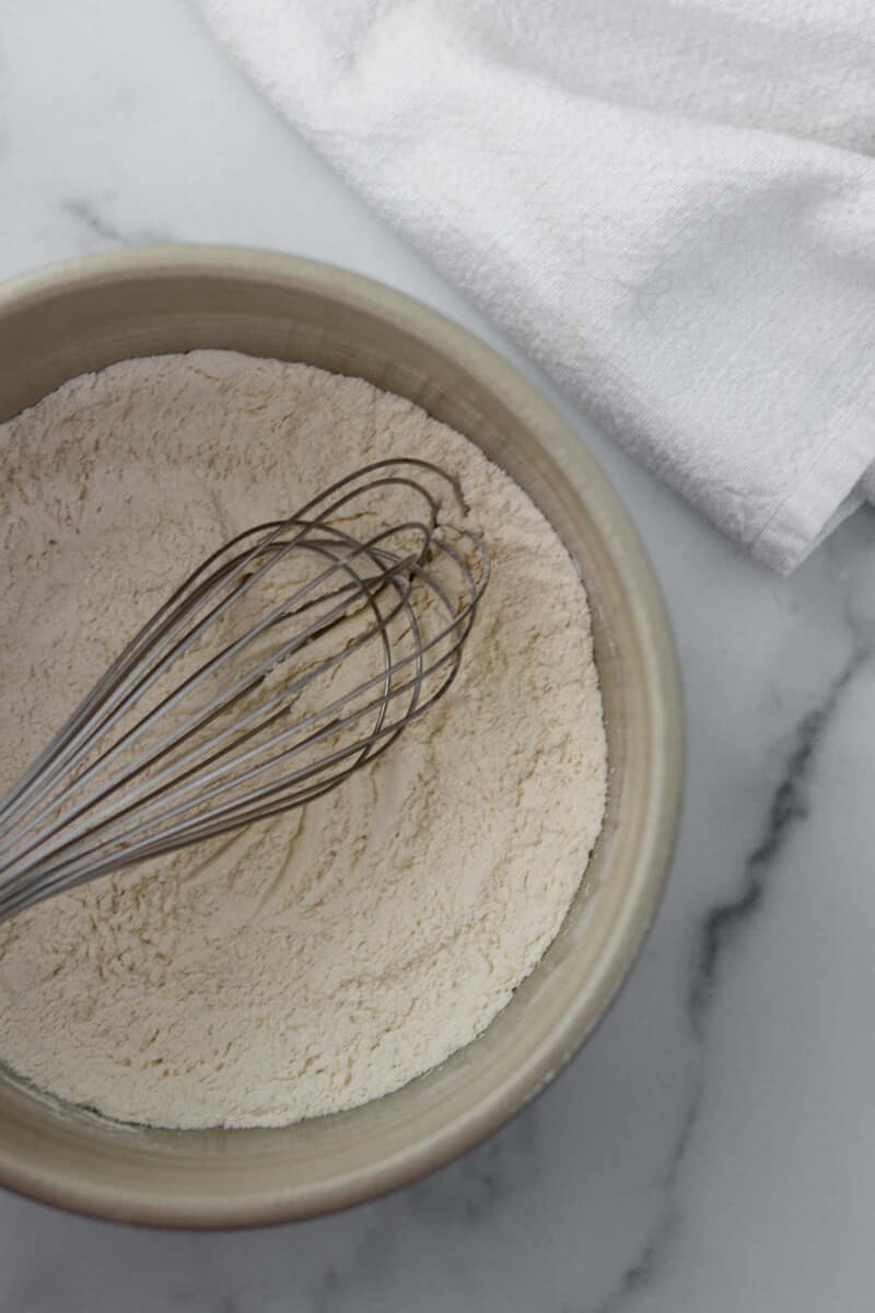 Flour in a bowl with a whisk on a marble background.