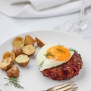 Beef Lindström on a plate topped with a fried egg next to roasted potatoes.