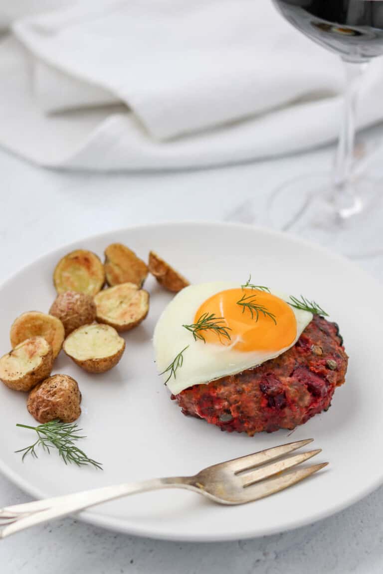 Beef Lindström on a plate topped with a fried egg next to roasted potatoes.