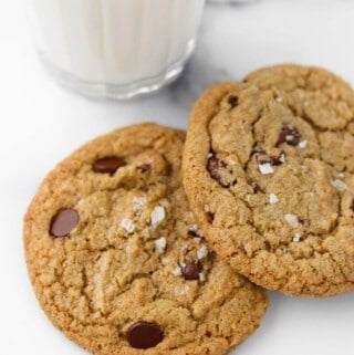 Two chocolate cookies on a marble surface next to a glass of milk.