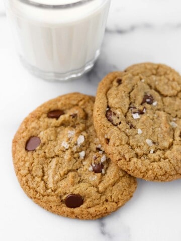 Two chocolate cookies on a marble surface next to a glass of milk.