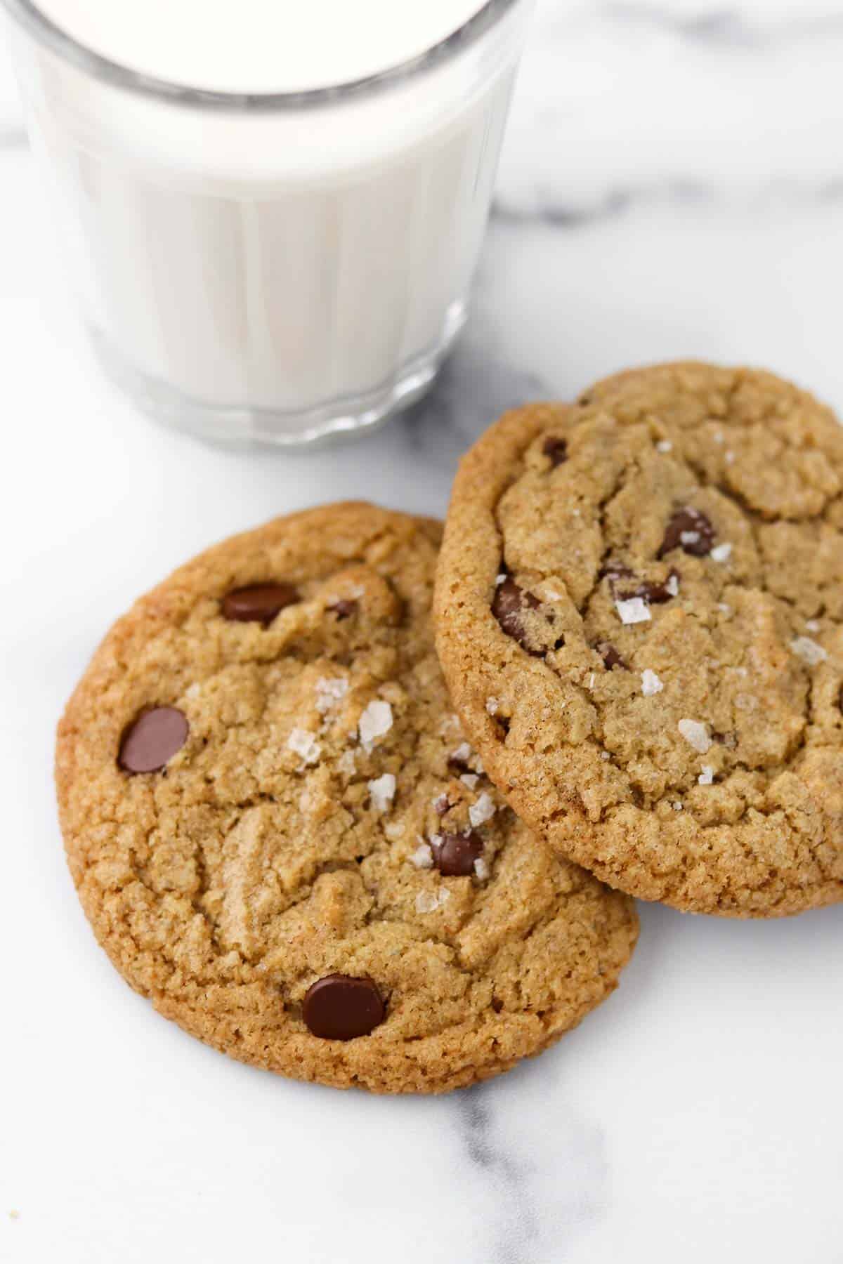Two chocolate cookies on a marble surface next to a glass of milk.