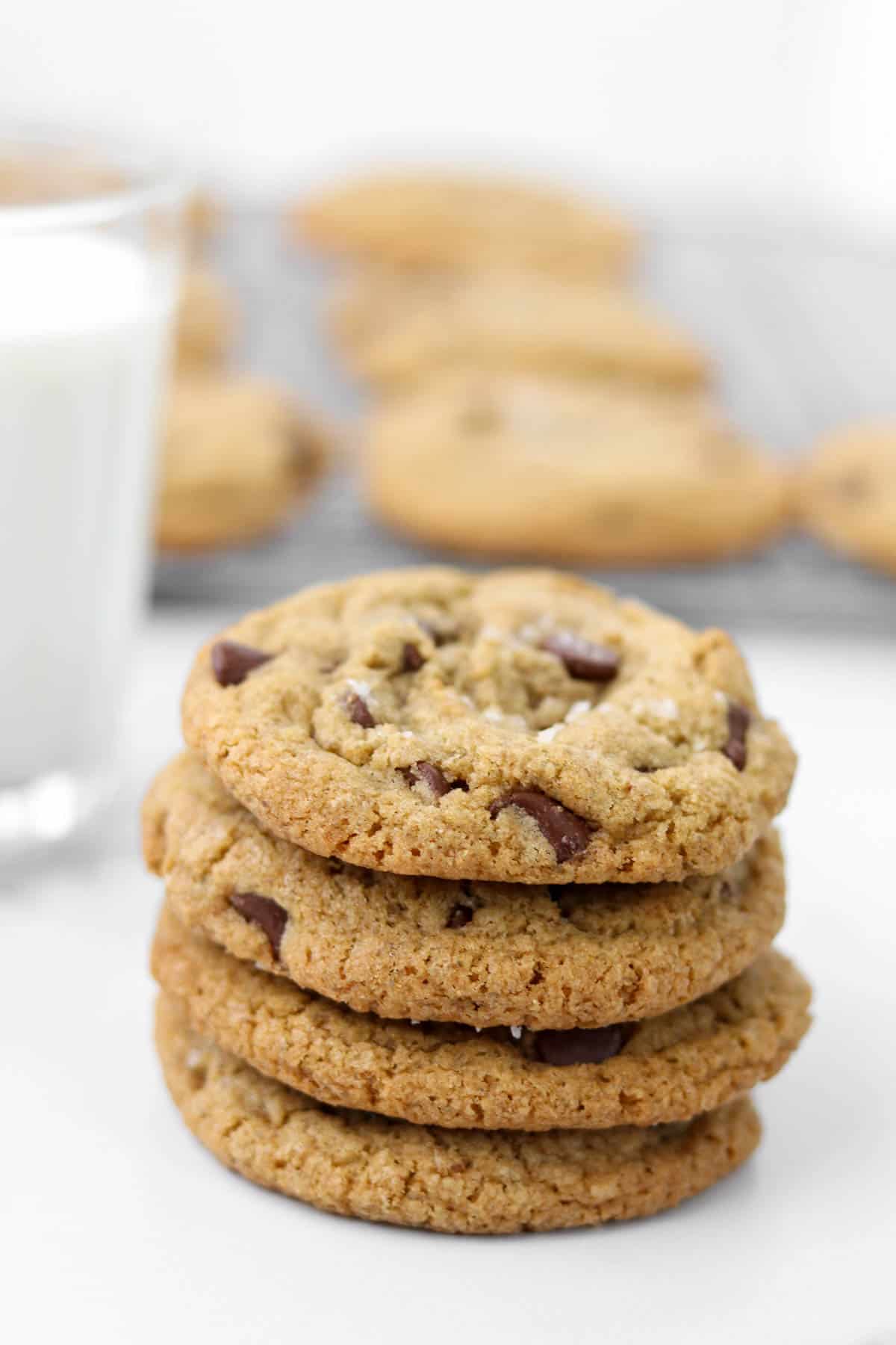 A stack of four chocolate chip cookies with a glass of milk.