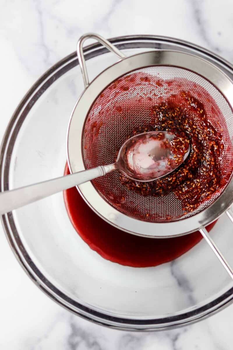 Raspberry jam in a strainer with a spoon.