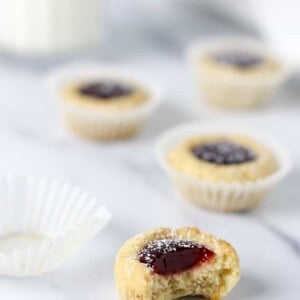 Raspberry thumbprint cookies on a marble surface with a glass of milk.