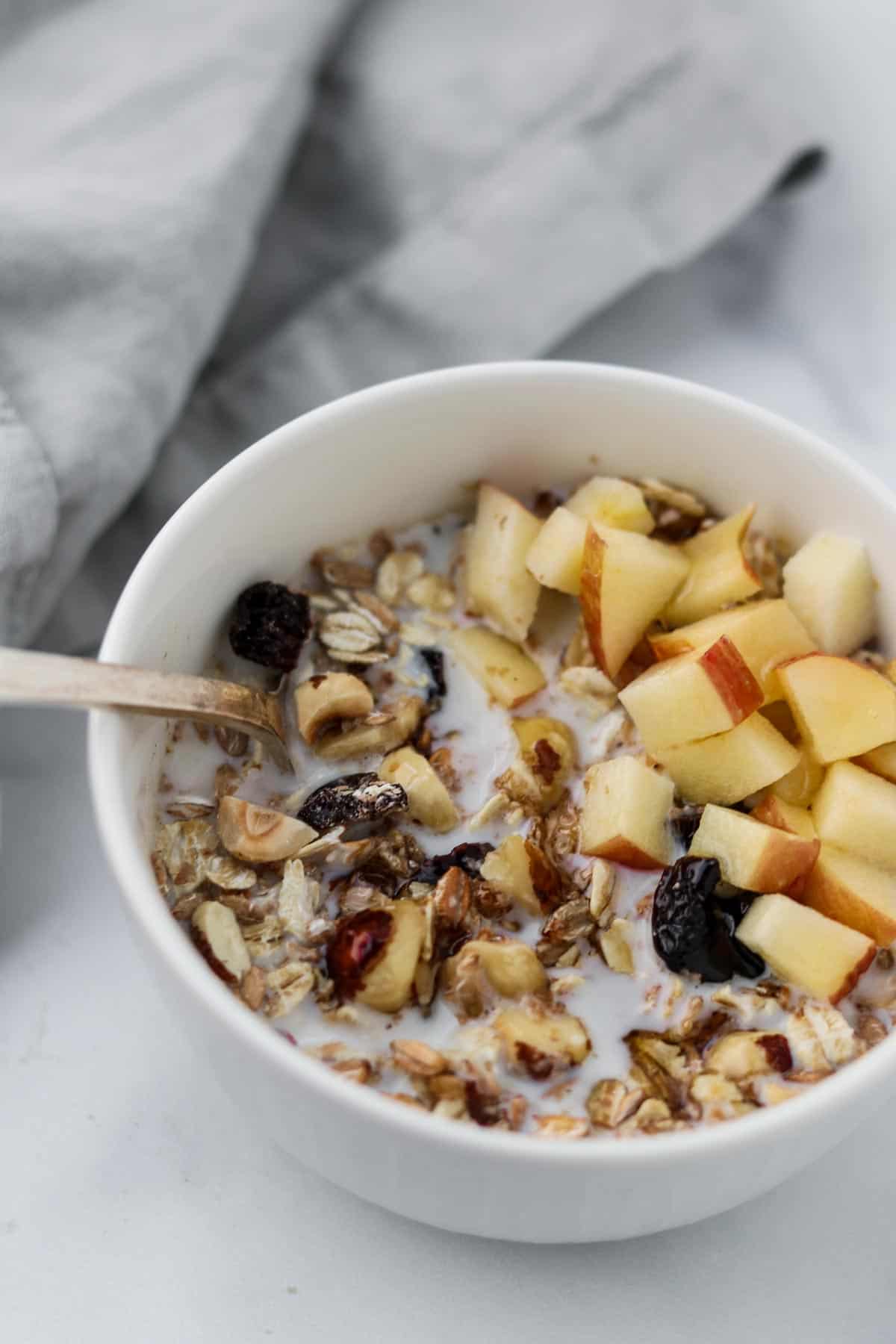 A bowl of muesli with chopped apples next to a napkin.
