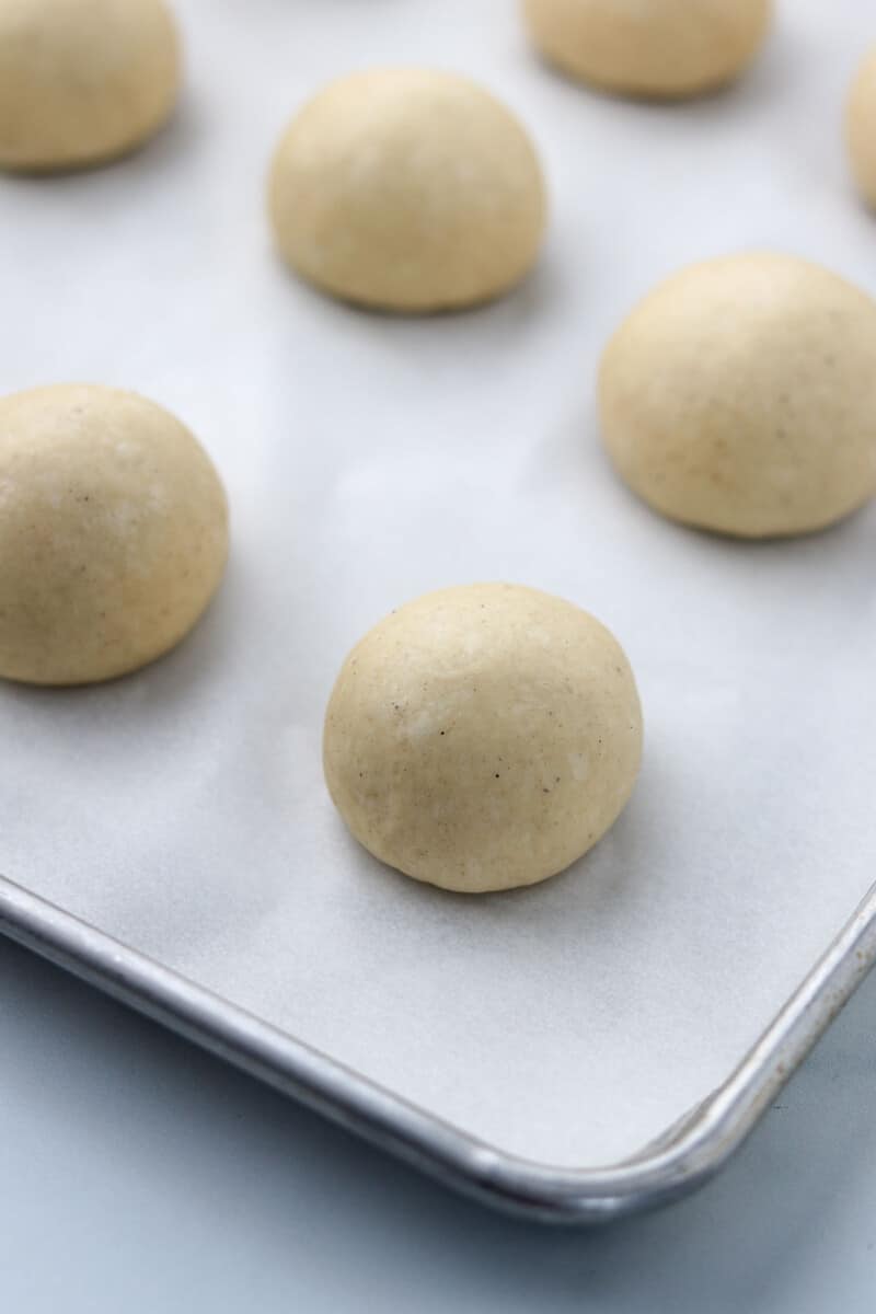 Unbaked round buns on a baking sheet.