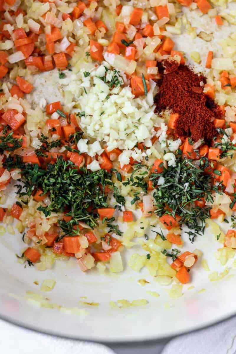 Chopped onions, carrots, garlic, herbs and spices in a pot.