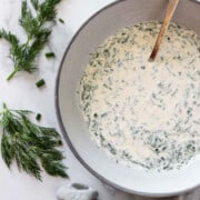 A bowl with herbed yogurt sauce next to fresh dill sprigs and a napkin.