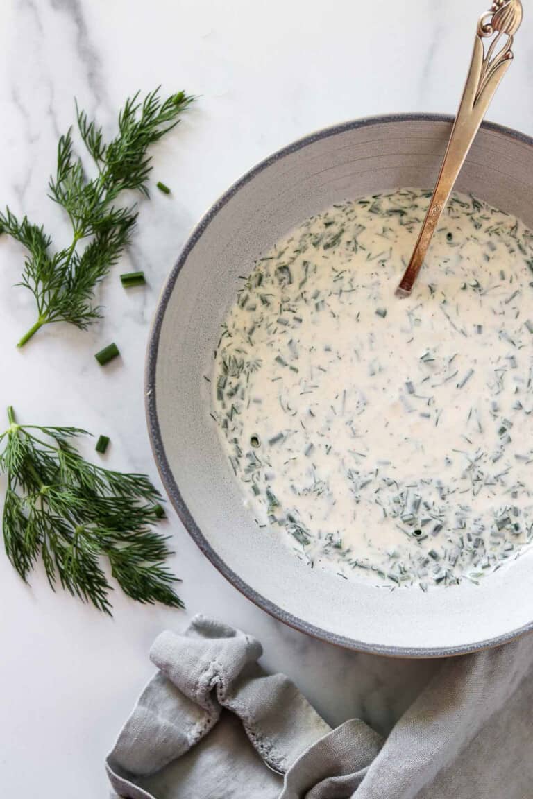 A bowl with herbed yogurt sauce next to fresh dill sprigs and a napkin.