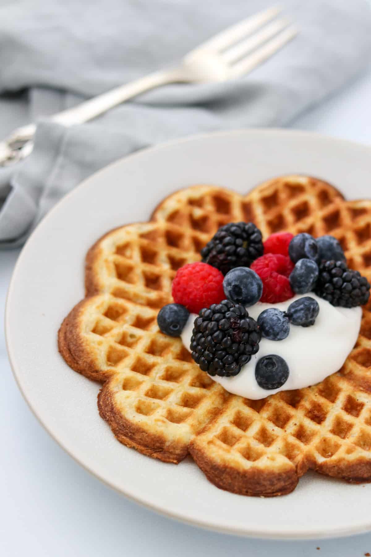 Heart shaped waffle on a plate topped with whipped cream and fruit.