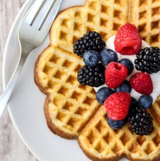 Heart-shaped waffle on a plate topped with whipped cream and fruit.