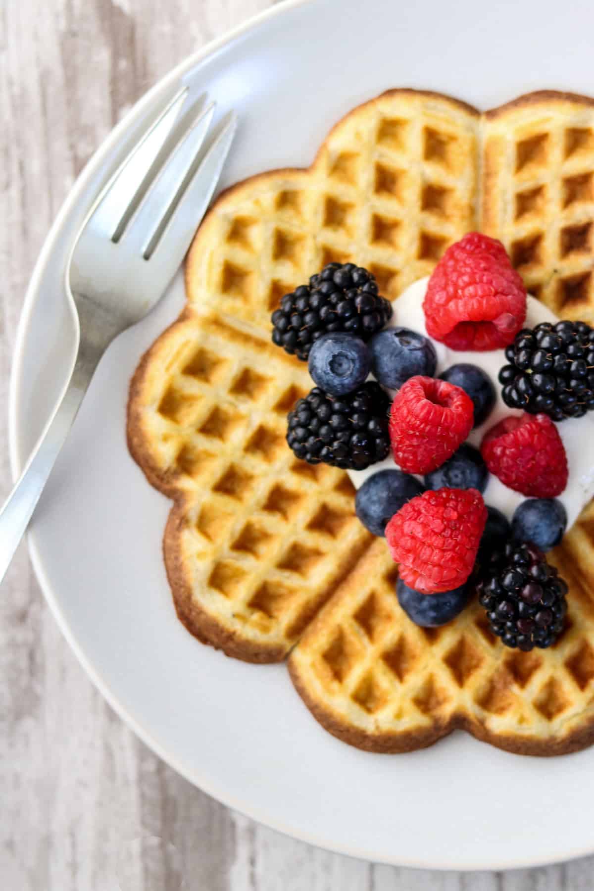 Heart-shaped waffle on a plate topped with whipped cream and fruit.