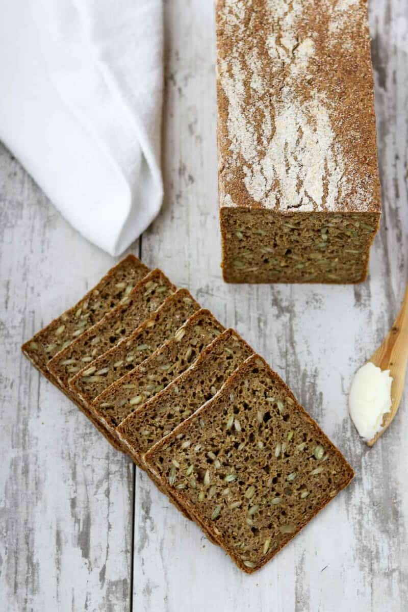 Sliced rye bread on a wood surface next to butter.