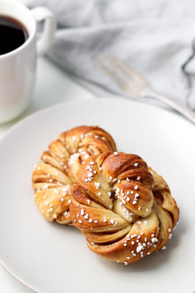 Swedish cinnamon buns on a plate next to a cup of coffee.