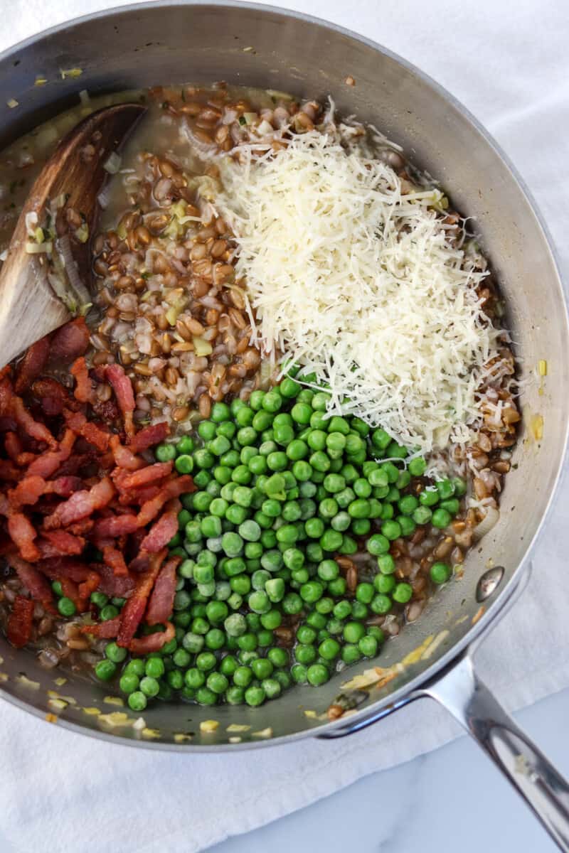 Rye berries, cheese, bacon and peas in a pan with a wooden spoon.