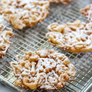 Funnel cakes dusted with powdered sugar on a wire rack.