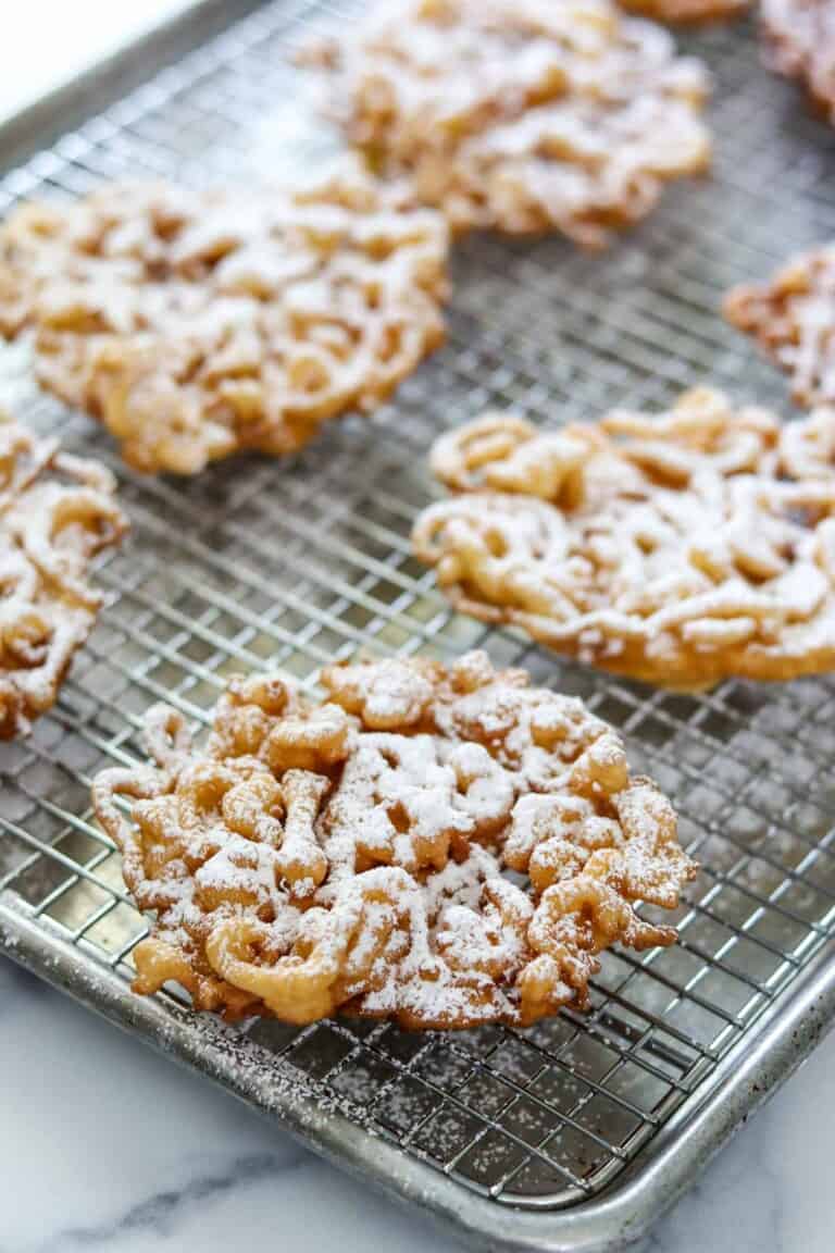 Funnel cakes dusted with powdered sugar on a wire rack.