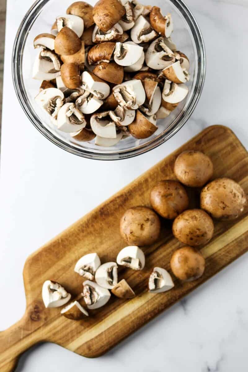 Cut mushrooms in a bowl next to a cutting board with mushrooms on top.