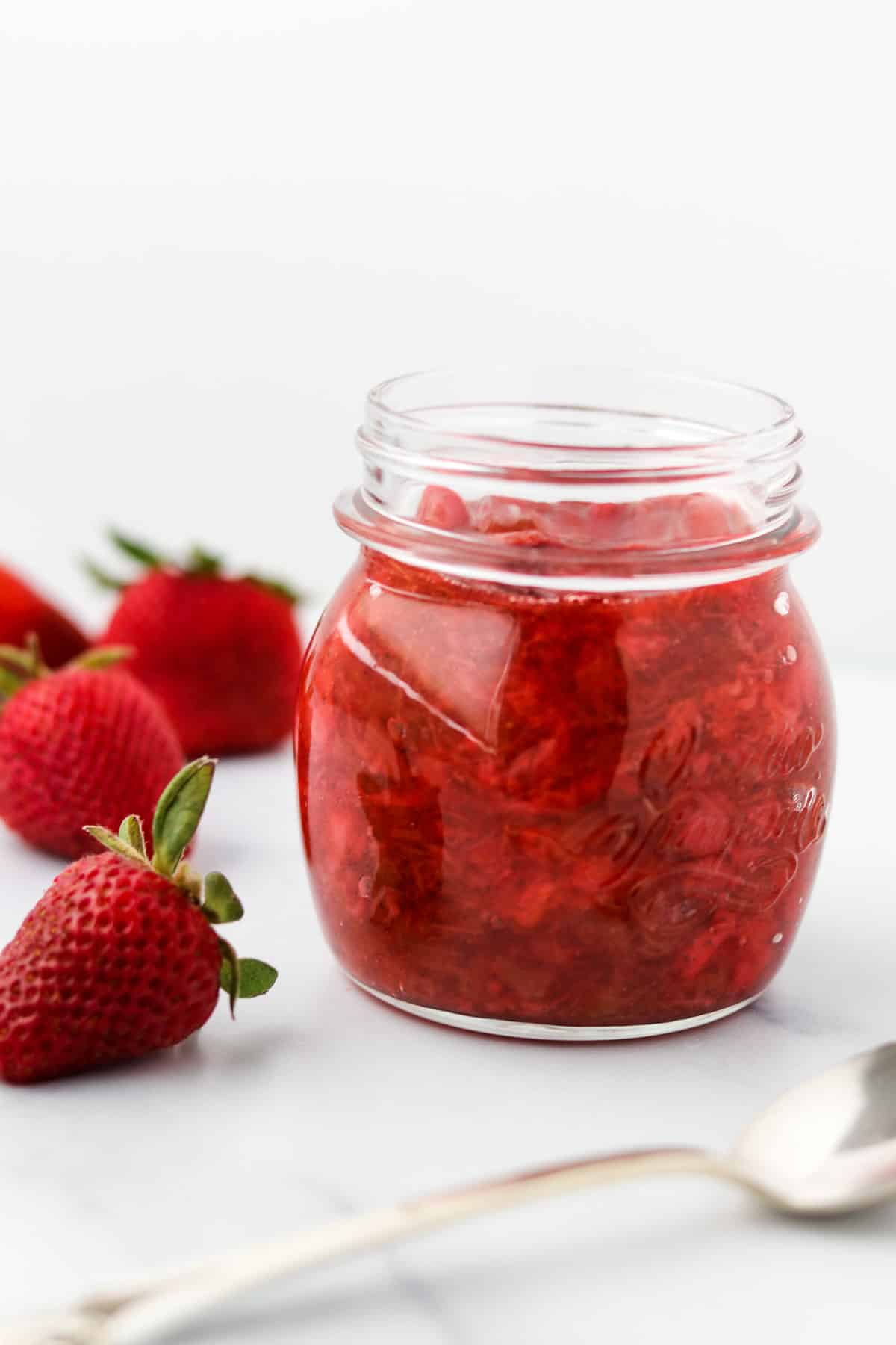 Jar of Roasted Strawberry Rhubarb Compote next to strawberries and a spoon.