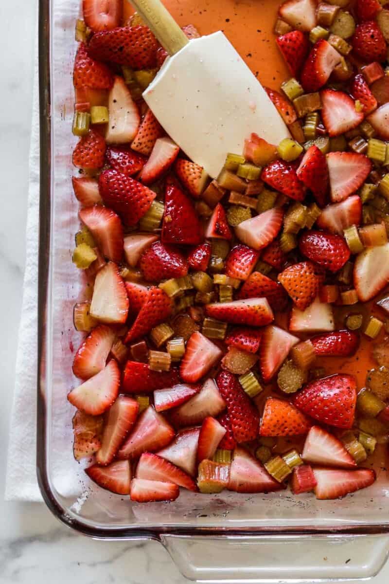 Strawberries and rhubarb in a baking dish with a rubber spatula.