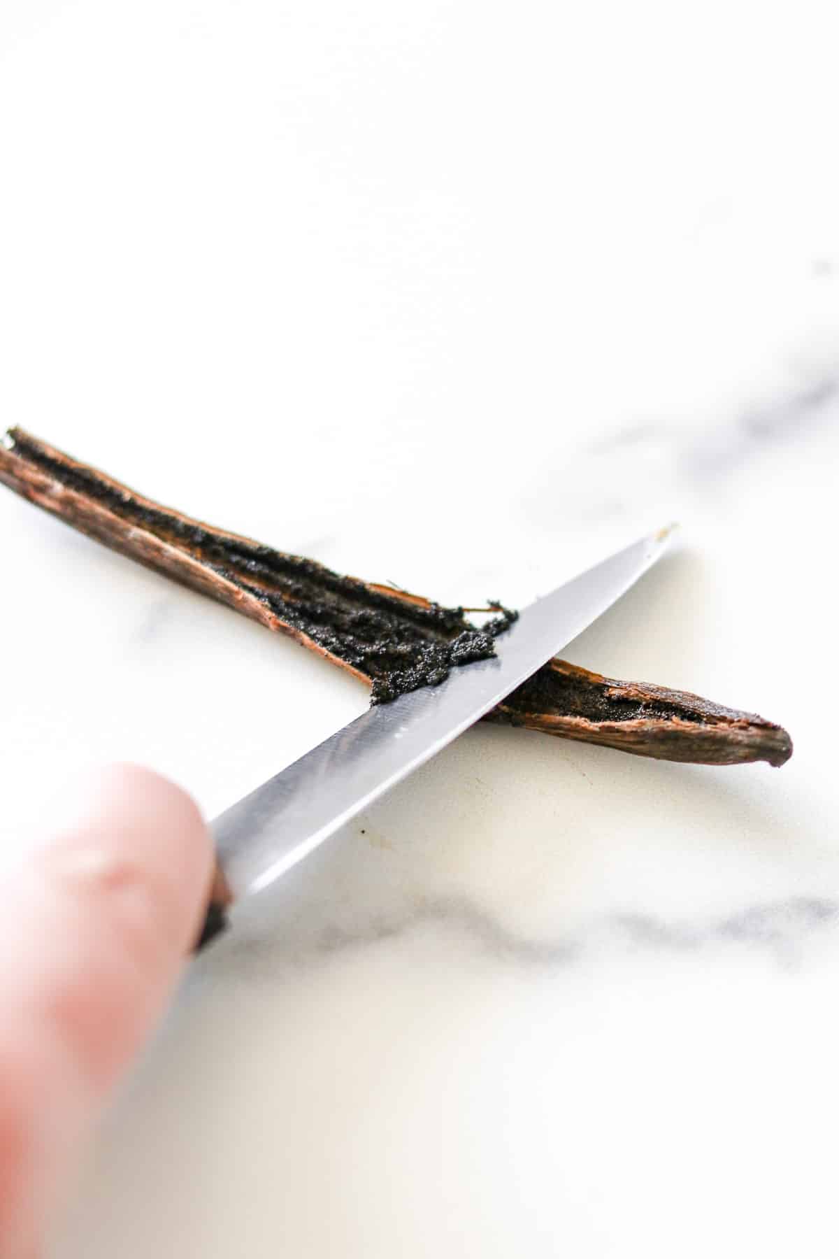 Close up of scraping out a vanilla bean with the back of a knife.