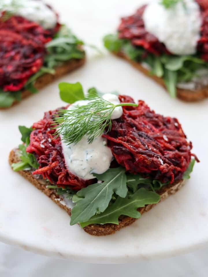 Beet and celery root cakes on rye bread with arugula and a creamy sauce.