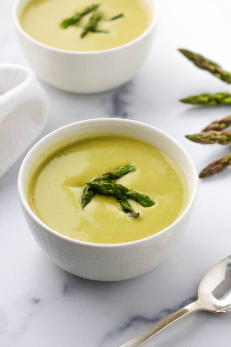 A bowl of Creamy Asparagus, Leek and Pea Soup next to a spoon.