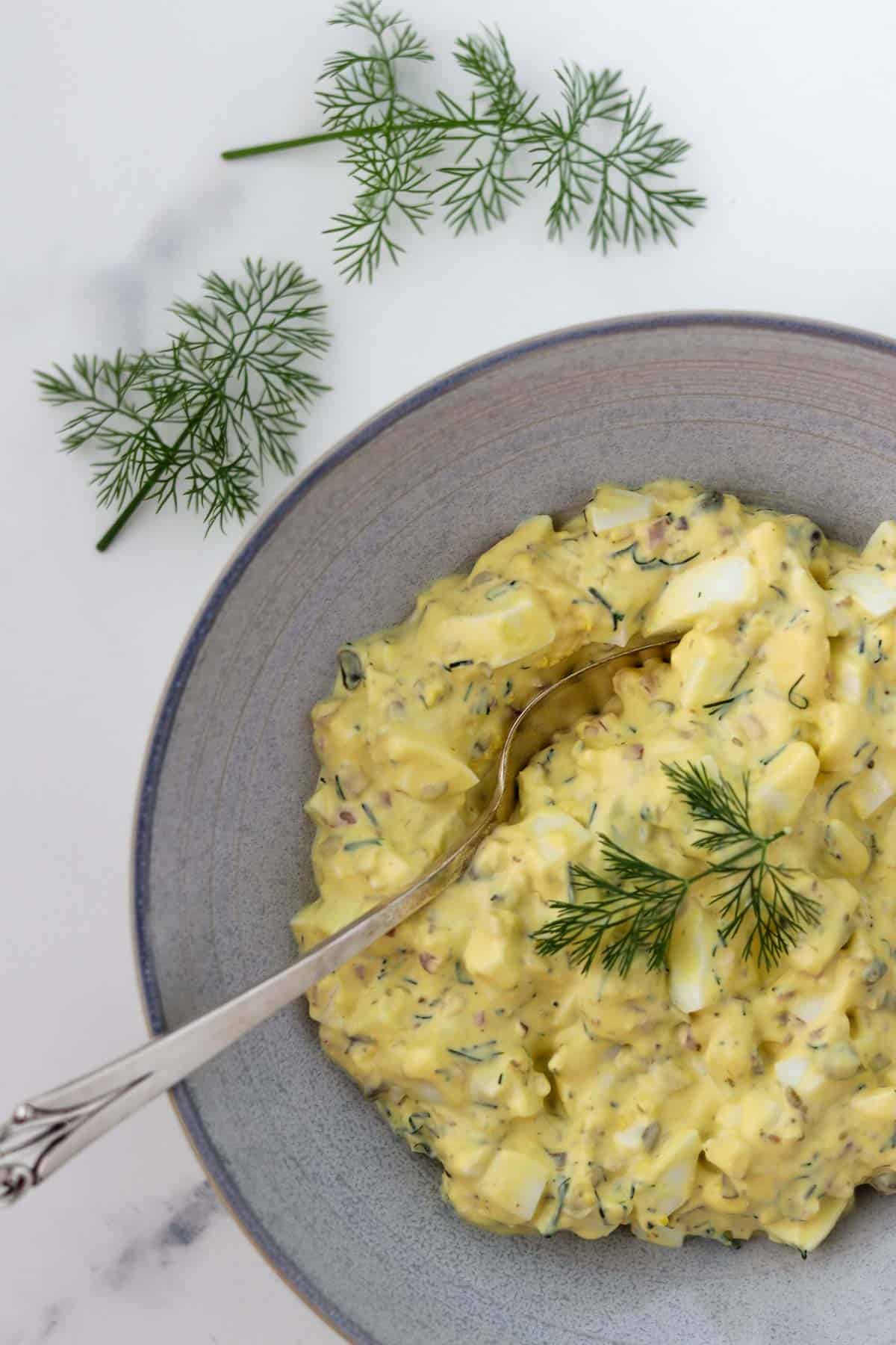 Egg Salad in a bowl with a spoon next to dill sprigs.