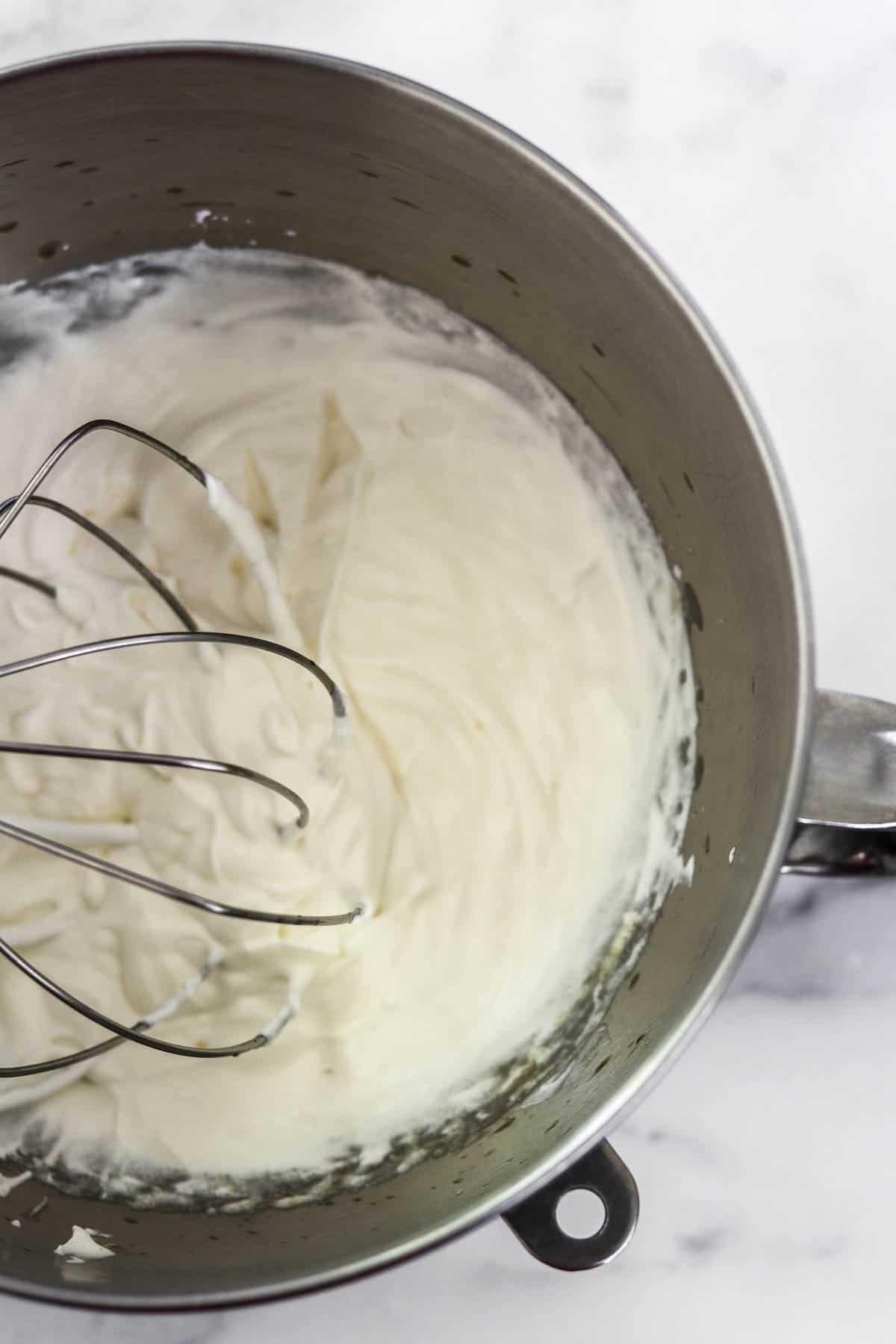 Whipped cream in a metal bowl with a whisk.