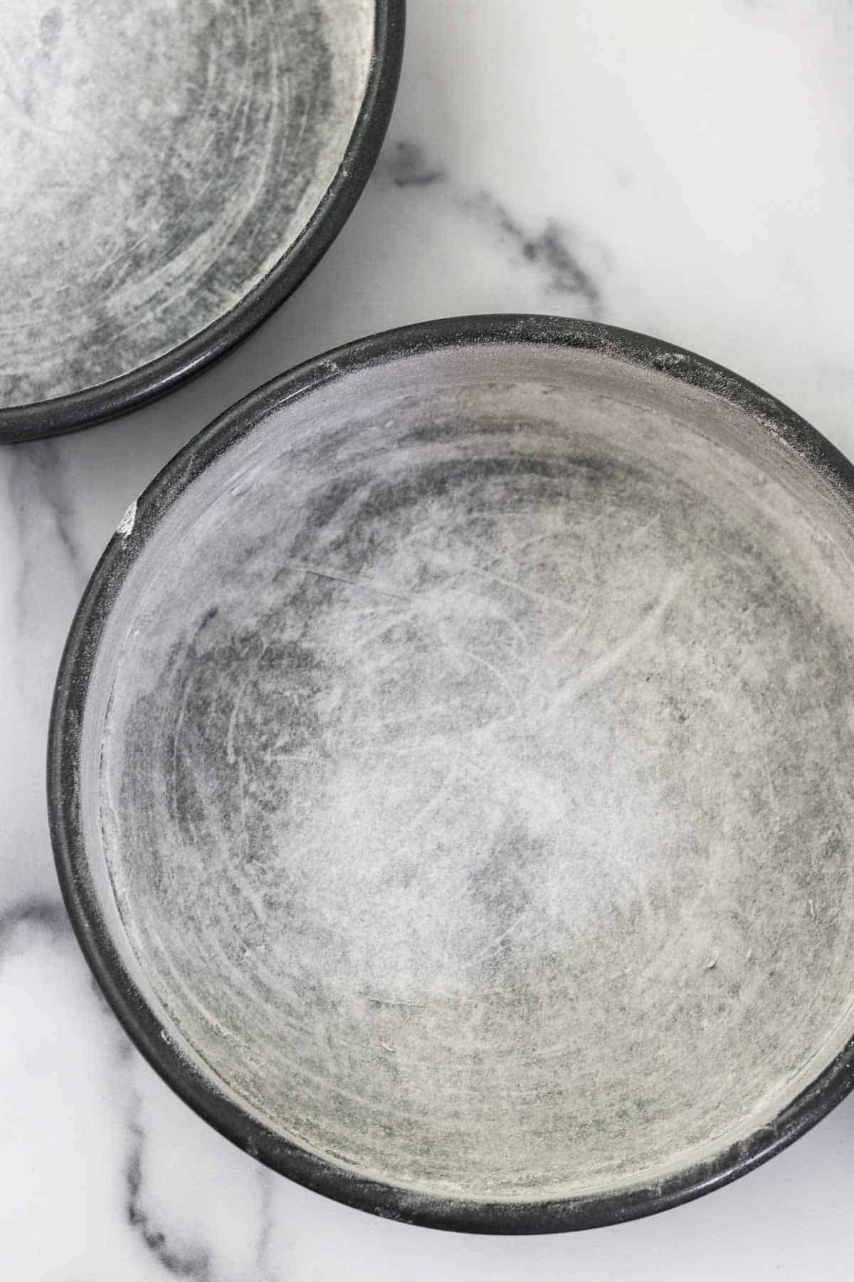 Greased and floured cake pans on a marble surface.
