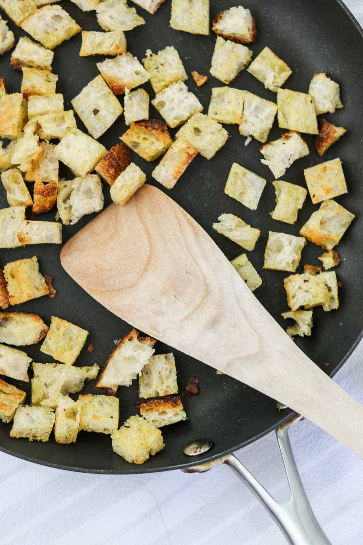 Croutons in a skillet with a wooden spatula.