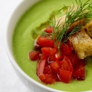 Close up of chilled cucumber soup with chopped tomatoes, croutons and dill on top.