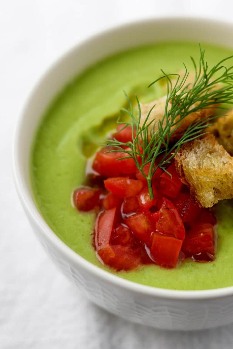 Close up of chilled cucumber soup with chopped tomatoes, croutons and dill on top.