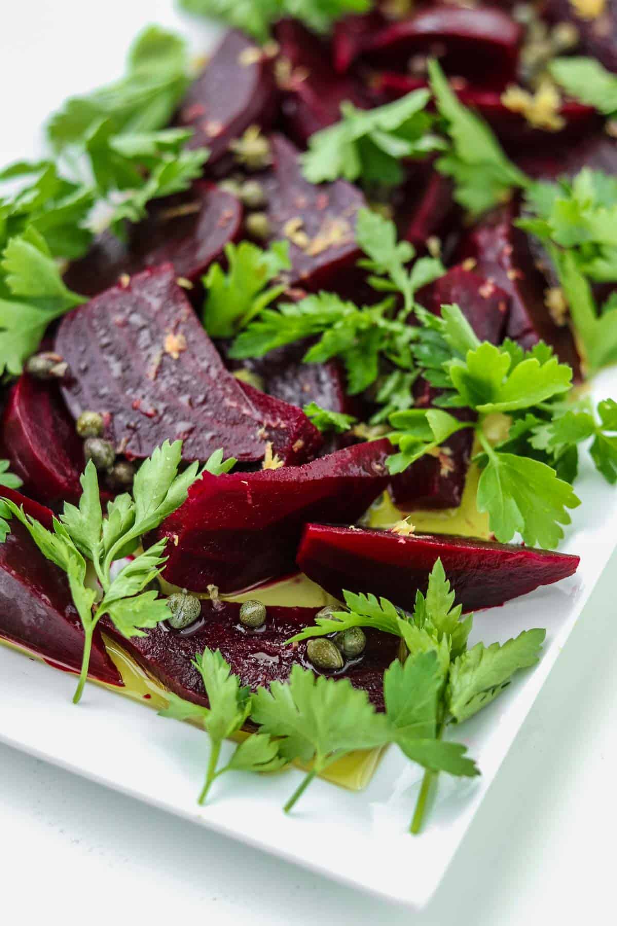 Beet salad on a white platter with parsley and capers.